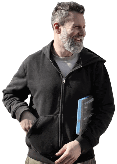 A man with a beard wearing a black hoodie and holding a book at home.