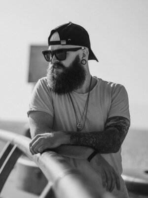 A man with a beard leaning against a home railing.