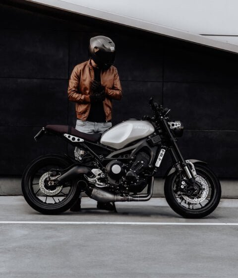 A man is standing next to a motorcycle at his home.