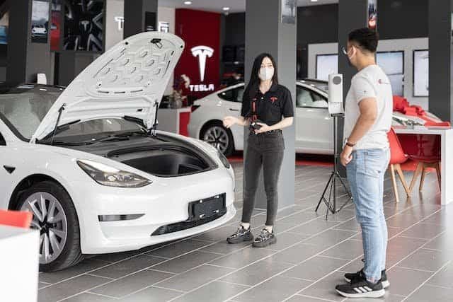 Two people standing next to a tesla model s in a showroom.