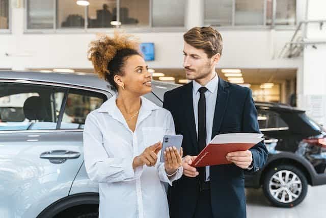 A man and woman standing next to a car in a dealership.